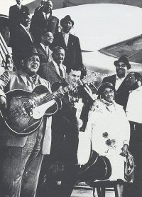 1963 AFBF ensemble, arrival at Frankfurt a.M. airport: from top: three airline company employees, Memphis Slim, Otis Spann, Muddy Waters, Bill Stepney, Sonny Boy Williamson; front row: Big Joe Williams, Len Kunstadt, Victoria Spivey, Willie Dixon; behind Willie Dixon: Matt 'Guitar' Murphy; source of photo on the right: Juke Blues 20 (1990), p. 10 '(courtesy 1968 AFBF programme)'