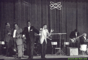 >American Folk Blues Festival 1963 at Salle Pleyel, Paris, France, October 5, 1963; (l to r) Willie Dixon, Big Joe Williams, Otis Spann (or Memphis Slim?) (hidden), Muddy Waters, Lonnie Johnson, Matt Murphy, Bill Stepney; source: Les Génies du Blues, Volume 2.- Paris (Editions Atlas) 1992, p. 113; photographer: Jean-Pierre Leloir