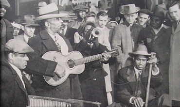 Original caption: 'The street surges to the rhythm of 'Stovepipe' Watson's band. The homemade instruments beat out frantic music that isn't good, but loud.' source: (Anonymous: 'Chicago Side Show: A Picture Pageant'.- Pageant Vol. 1, No. 4 (March 1945), pp. 45-52