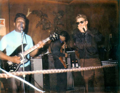 Muddy Waters, Luther 'Georgia Boy' Johnson (with his back to the camera) and Paul Oscher at Helen Hermes' Moonlight Lounge on Goode Ave [now Annie Malone Dr] in St Louis, Missouri, c. 1968; Photo, taken by a Polaroid photographer in the club, posted at facebook by Paul Oscher (07/14/2019), photoshop embellished by Stefan Wirz